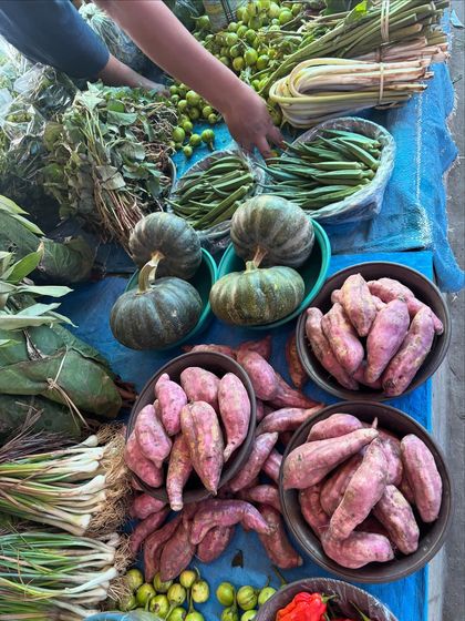 A colorful assortment of local produce, including purple sweet potatoes, small green pumpkins, and wild herbs, all sourced directly from Naga farmers.