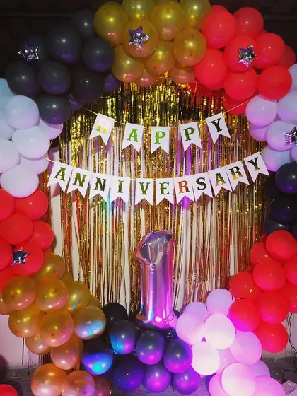 A first-anniversary celebration with a full balloon ring in red, black, white, and gold, set against a gold shimmer curtain.