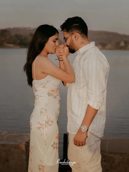 A gentle and intimate moment where the groom kisses the bride's hand as they stand by the water at sunset.