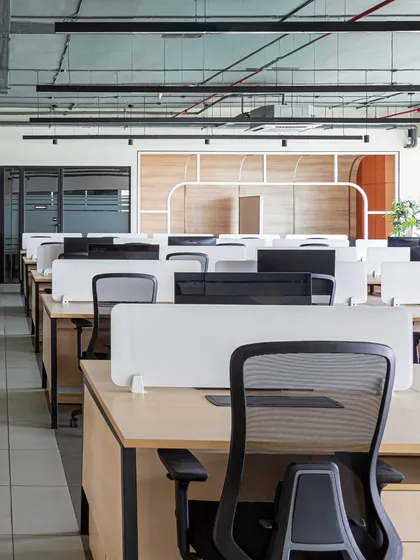 From this angle, you can see the collaboration zone framed in the background, a signature element of the office. The workstations are kept clean and uniform to create a sense of order and focus.