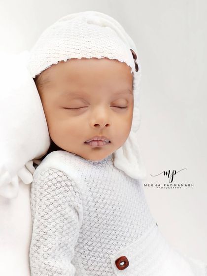 A baby boy in a white textured romper and matching hat, sleeping peacefully.