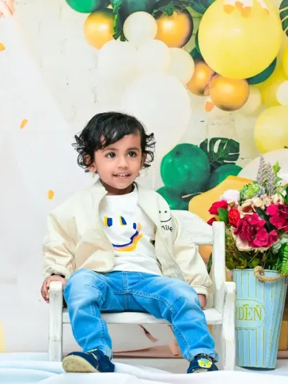 A wider shot of the second birthday setup, showing the toddler looking off to the side against a backdrop of green and yellow balloons. This captures a candid, unposed moment during the session.