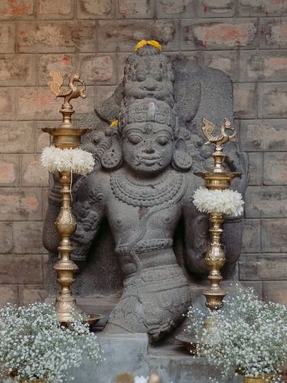 An ancient stone idol decorated with jasmine garlands and brass lamps, creating a sacred focal point.