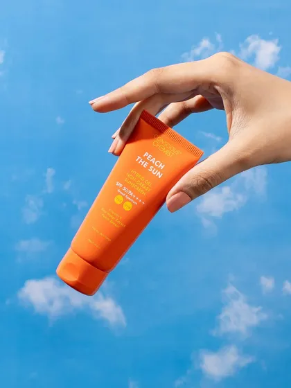 This shot uses a hand model to showcase the sunscreen against a bright blue sky backdrop. The composition makes the product feel like an essential part of a perfect summer day.
