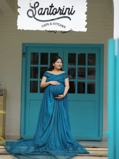 A beautiful solo portrait in our teal maternity gown. The off-shoulder design and long train create an elegant silhouette against the iconic blue and white background.