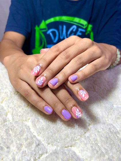 A cute and simple design on natural nails, with a mix of solid lavender and a delicate white leaf pattern on a pink base.