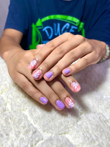 A cute and simple design on natural nails, with a mix of solid lavender and a delicate white leaf pattern on a pink base.