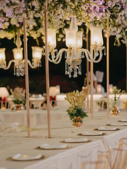 A closer view of a luxurious tablescape, with vintage-style chandeliers hanging above the table. The warm light and floral decor create an intimate and opulent dining experience.