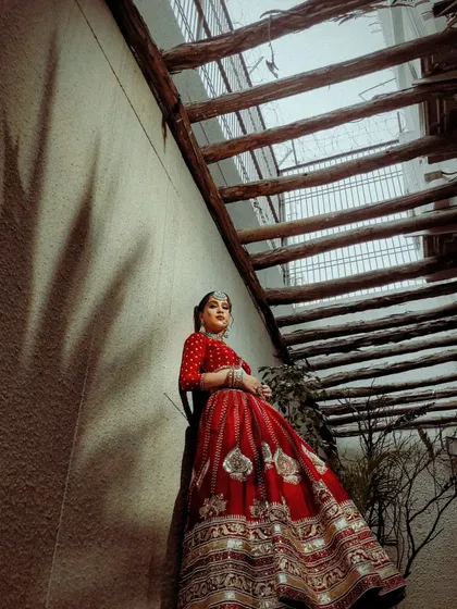 An artistic shot of a bride in a red lehenga. The play of light and shadow highlights the texture and rich color of the traditional outfit I styled.