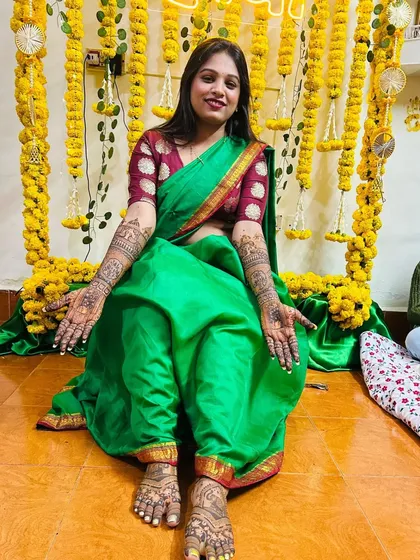 A happy bride showing off her complete mehndi look, including her beautifully adorned feet. The design is traditional and complements her Maharashtrian bridal attire perfectly.