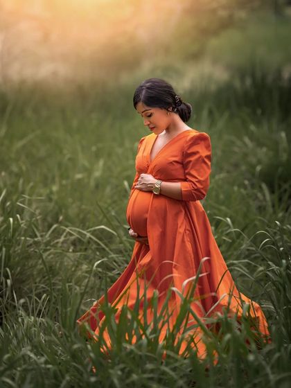 A duplicate of ID 33, this solo outdoor portrait captures an expecting mother in a vibrant orange dress amidst tall green grass, with soft, golden light giving it a dreamy quality.