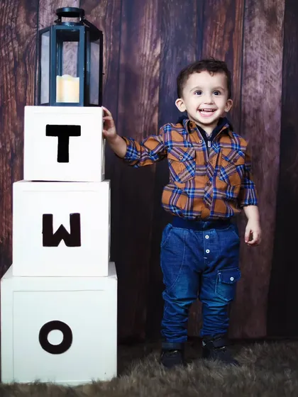 A proud two-year-old stands next to his birthday blocks, smiling for the camera.