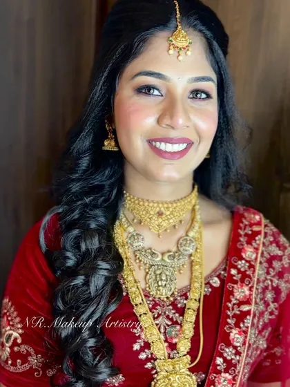 A smiling bride ready for her reception. Her makeup is fresh and glowing, complementing her red lehenga and gold jewelry.