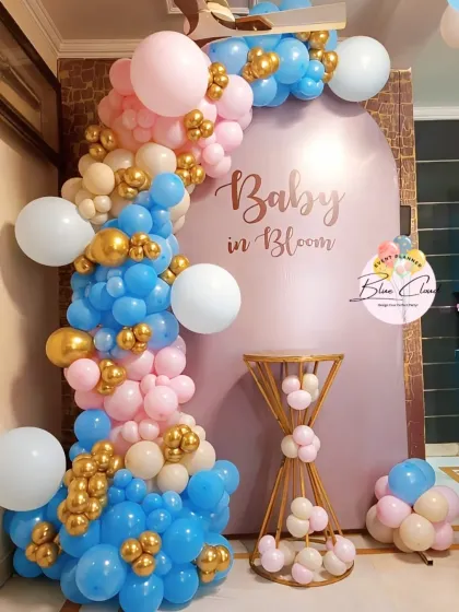 A 'Baby in Bloom' themed setup with a custom arched backdrop and an organic balloon garland in pink, blue, and gold.
