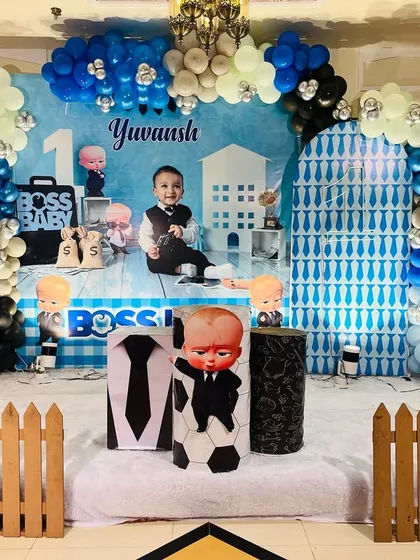 A full stage setup for a classic Boss Baby first birthday party. I used a custom-printed backdrop with the child's name, multiple character cutouts, a themed balloon arch in blue, black, and silver, and a small picket fence to complete the look.