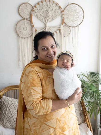 A proud grandmother smiling as she holds her swaddled newborn grandchild. Capturing these moments with extended family is an important part of my newborn sessions.