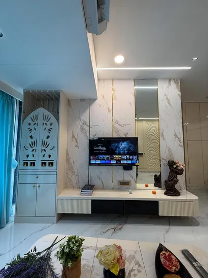 A glimpse of a finished living room in Mumbai, integrating a custom TV unit with marble-finish panels and a beautifully crafted pooja mandir with jaali work. The design balances modern aesthetics with traditional values.