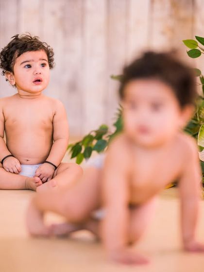 A minimalist and natural setting for twin portraits. The simple wooden floor and fresh greenery allow the focus to remain entirely on the babies, perfect for newborn or crawler-stage photos.