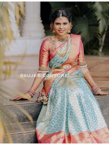 A modern Langa Voni for a stylish bride. She is seated on steps, showing off the flow of her light blue patterned skirt paired with a contrasting pink and gold blouse with bell-sleeved details.