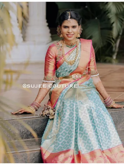 A client looking elegant in a custom-designed half saree. The powder blue brocade skirt is paired with a contrasting pink blouse, featuring delicate bell-shaped tassels on the sleeves.
