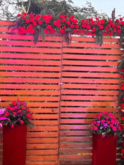 A rustic wooden photo wall decorated with red flowers. This provides a great textured backdrop for guest photos and can be part of a larger red-themed wedding decor.