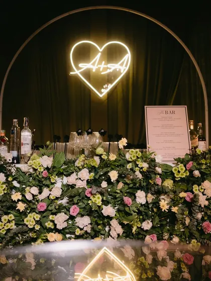 The bar for the "Big Bow Affair," featuring a custom neon sign with the couple's initials and a lush floral base.