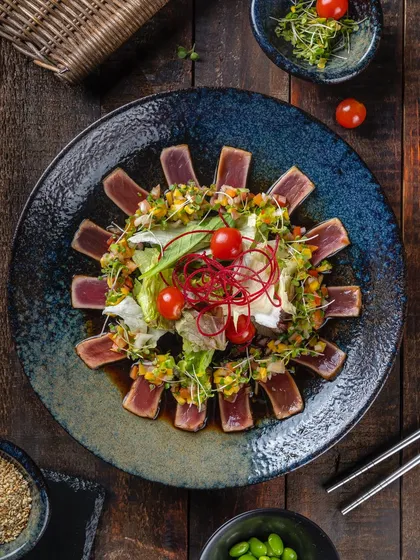 A modern presentation of tuna tataki salad for Hahn's Kitchen, arranged in a sunburst pattern on a dark, textured plate.