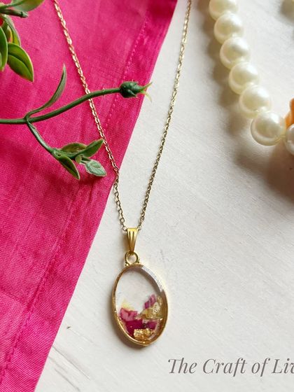 An oval-shaped pendant with preserved pink petals and gold flakes. The classic shape makes it a timeless piece that can be worn for any occasion.