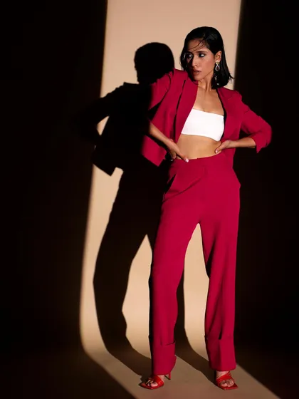 A full-length shot of a vibrant red pantsuit, styled with a simple white bandeau. The dramatic lighting and strong pose emphasize the suit's modern cut and powerful color.