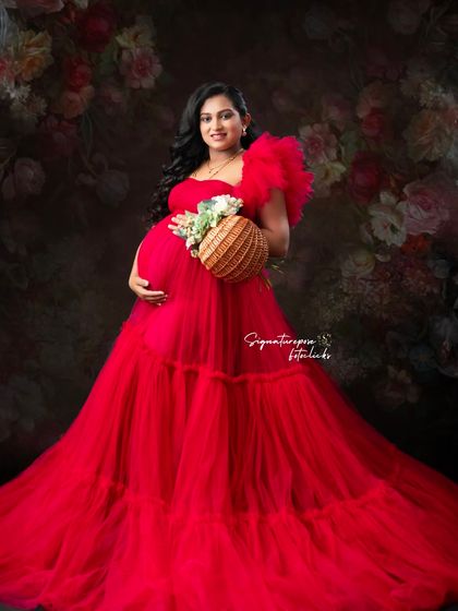 A stunning portrait against a dark floral backdrop, where the red gown and the mother's glow truly stand out.