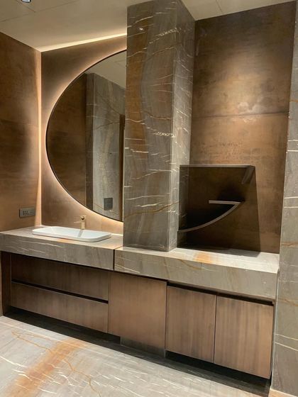 A bathroom vanity crafted from richly veined marble and warm wood tones. The backlit circular mirror and minimalist fixtures create a spa-like atmosphere of refined luxury.