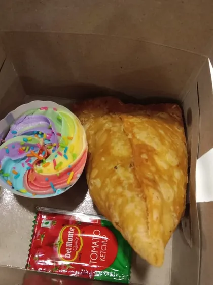 A snack box prepared for an event, featuring one of our rainbow cupcakes alongside a savory samosa and ketchup. A perfect balance of sweet and savory.