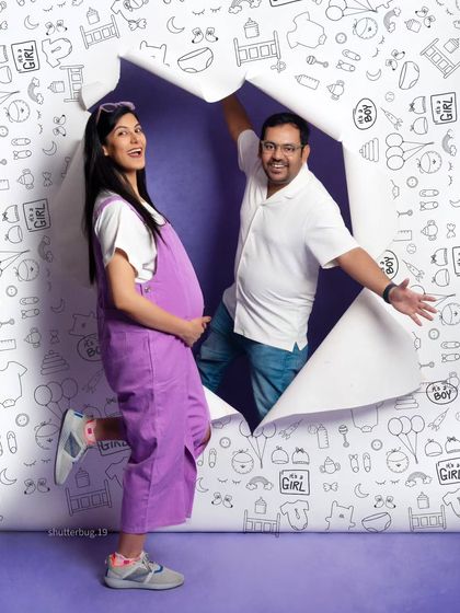 The couple playfully emerges from the torn paper backdrop. This dynamic shot is full of energy and excitement, making for a great pregnancy announcement photo.