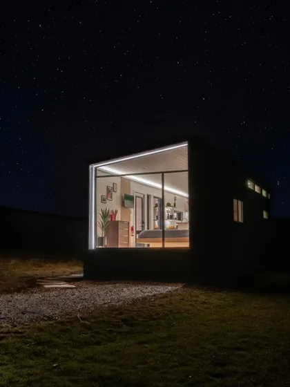 A view of our modular home at night, glowing like a lantern in the dark. This image highlights the dramatic effect of our designs and their connection to the surrounding landscape.