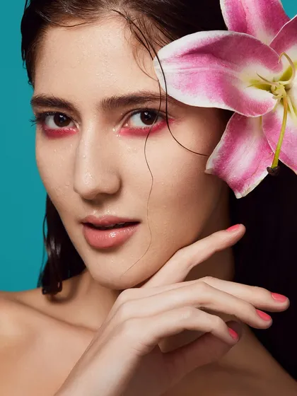 A wet-look makeup style with a pop of pink on the lower lash line, paired with a fresh lily and dewy skin.