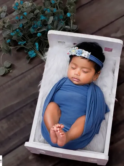 This little one is curled up and sleeping in a miniature white bed, wrapped in a beautiful blue swaddle.