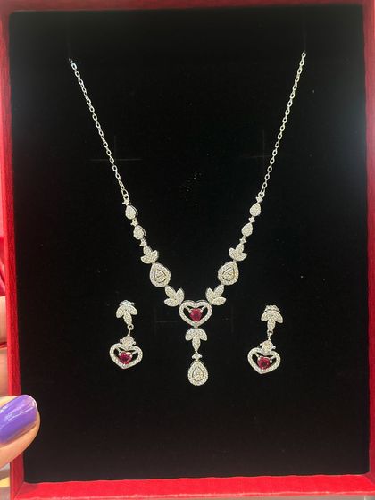 A heart-shaped ruby-red stone is the centerpiece of this lovely silver necklace and earring set. It's a perfect gift for a loved one.