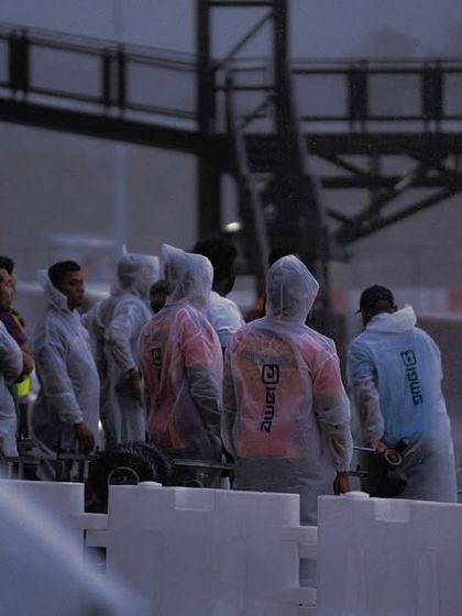 The team watches anxiously from the pit wall during a rain-soaked race.