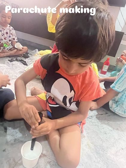 A child is carefully constructing his own parachute. This activity was part of our STEAM session on gravity, where we explored Isaac Newton's famous apple and why objects fall at different speeds.