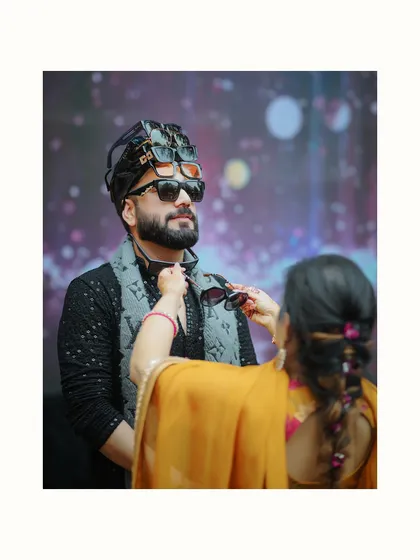 A quirky and fun shot of the groom getting ready for the Haldi, with his friends piling sunglasses on his turban.