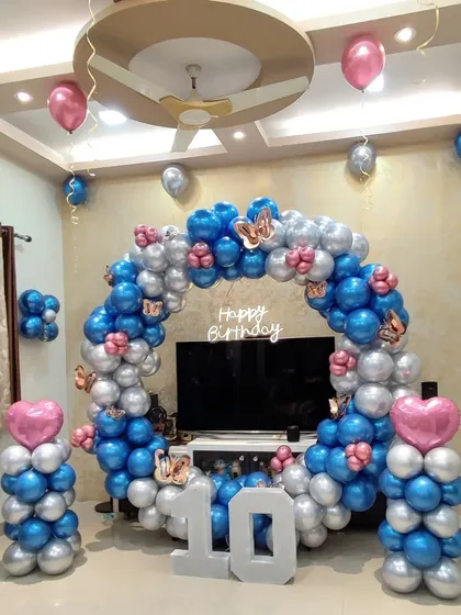 A 10th birthday celebration with a butterfly theme. The circular balloon arch is made of blue and silver chrome balloons, accented with butterfly cutouts and a large number '10' in front.