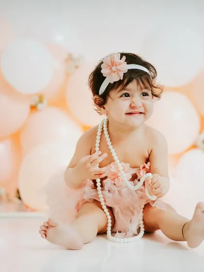 A shy smile from this little darling. The soft pastel pink balloons create a dreamy, gentle background for her first birthday portraits.