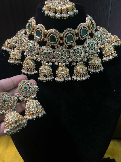 This image shows the beautiful detail of the choker necklace with its dangling jhumkas and pearl accents. It's a high-quality piece that looks heavy but is designed to be comfortable to wear throughout the event.
