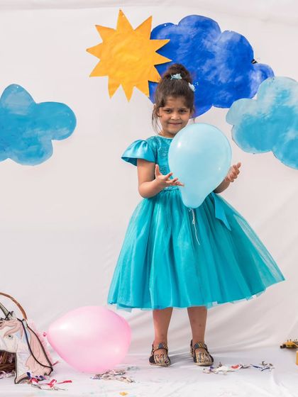 A happy girl ready to celebrate in her bright blue tulle dress. The flutter sleeves and full skirt are made for movement, ensuring she’s comfortable while looking absolutely adorable.