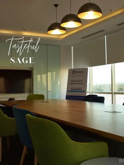 A tasteful and sage conference room. The large wood table is surrounded by chairs in muted green and blue tones, creating a professional yet stylish meeting space.