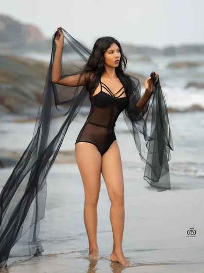 A full-length shot of the model walking on the beach, with the sheer black fabric trailing behind her. The movement and the beautiful coastal scenery make for a cinematic image.