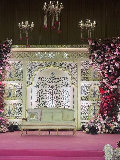 A wider perspective of the ornate wedding stage, highlighting the cascading floral pillars and the beautiful 'tree of life' motif in the backdrop. The design balances grand floral statements with delicate traditional artistry.