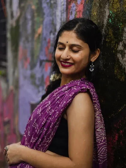 A candid portrait filled with warmth. The model leans against a colorful wall with her eyes closed and a gentle smile, capturing a moment of pure contentment during our monsoon-themed shoot.