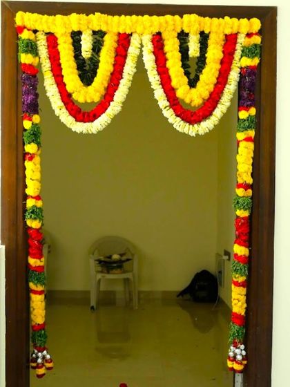 A traditional housewarming decoration for a main door. The door is framed with garlands of yellow, red, and black flowers for a colorful welcome.