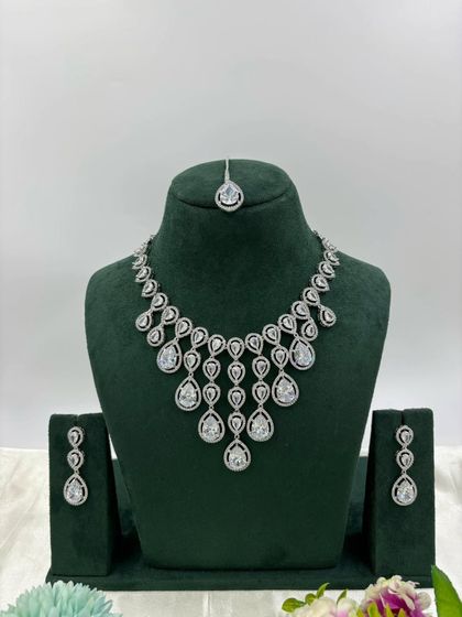 An elegant AD necklace set with a matching maang tikka. The cascading design with teardrop stones is available in green, pink, and all-white, perfect for receptions and parties.